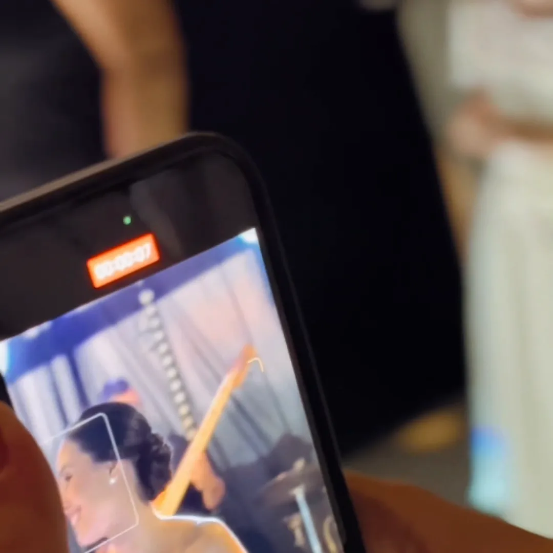 IMAGEN: plano de las manos sosteniendo el celular en vertical con la fiesta en pantalla — nadie mirando a cámara